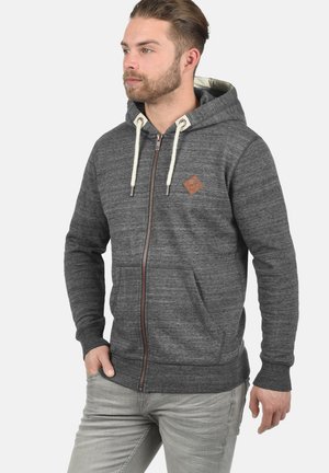 Sudadera con cremallera de felpa gris, con cordones en crema, bolsillos laterales y un pequeño parche de logo marrón en el pecho. Presenta puños y dobladillo de canalé.