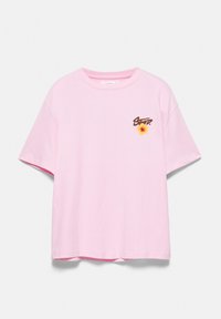 T-shirt rose clair à manches courtes avec un petit texte brun "STORY" et un motif de fleur jaune sur le côté gauche de la poitrine sur fond blanc.