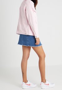 Chaqueta de denim rosa con detalles desgastados, combinada con una falda de denim azul con dobladillo deshilachado y zapatillas Nike blancas con acentos rosas.
