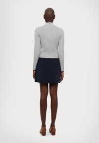 Maglione grigio a coste con collo alto e cerniera sul retro, abbinato a una mini gonna blu navy con due tasche posteriori. Scarpe con tacco marroni.