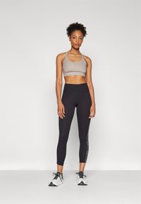 Sportssbrystholder i lys grå med mønstret tekstur, svarte høyt liv leggings med side logo print, kombinert med hvite treningssko.