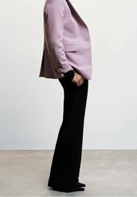 Blazer violet lavande cintré avec un seul bouton et des revers crantés, associé à un pantalon noir ajusté. Tissu lisse, silhouette structurée.