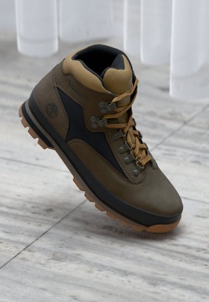 Bota de senderismo marrón hecha de ante y malla, con un diseño de caña alta, ojales de metal y una suela de goma con un agarre texturizado.