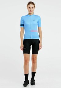 Blauw fietsshirt met korte mouwen, rits aan de voorkant, zwarte accentstrepen, gecombineerd met zwarte gewatteerde shorts en zwarte fietsschoenen.