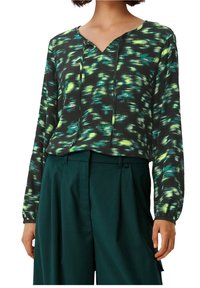 Langärmlige Bluse in Schwarz mit grün-und blauem abstraktem Muster. Verfügt über einen V-Ausschnitt und eine lockere Passform. Kombiniert mit dunkelgrünen Hosen.