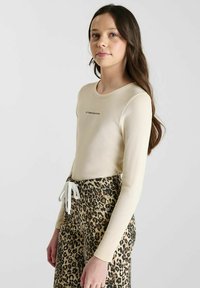 Haut beige clair à manches longues avec un col arrondi et une texture côtelée subtile, associé à un pantalon à imprimé léopard brun avec cordon de serrage.