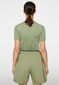 Oliivinvihreä urheiluasu, johon kuuluu lyhythihainen paita ja polven ylle ulottuvat shortsit, joissa on teksturoitu vyötärö ja joustavuus mukavuutta varten.