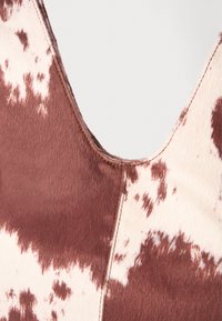 Close-up de tecido de pele de vaca castanho e branco com costura visível e um decote em V.