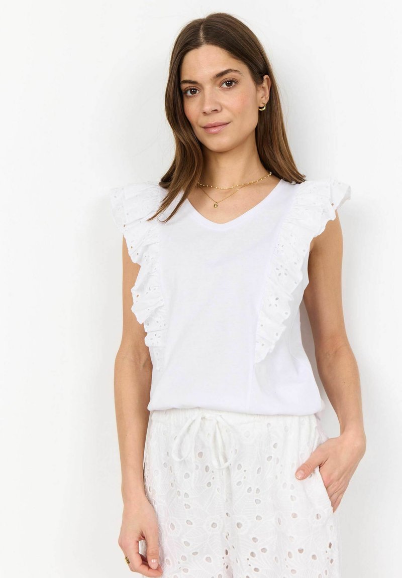 Vit ärmlös topp med broderad volangkant längs axlarna, med en v-ringning. Matchad med vita broderade shorts.
