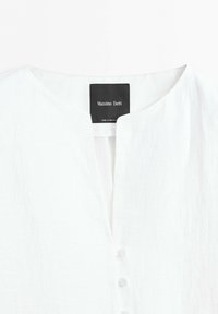 Bílá lněná blůza s kulatým výstřihem, zapínáním na knoflíky vpředu a černou etiketou Massimo Dutti přišitou uvnitř límce.