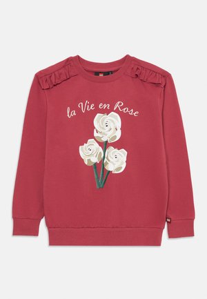 Rode sweatshirt met geribde manchetten en halslijn, met een bloemenpatroon van witte rozen en de tekst "la Vie en Rose." Met gerimpelde schouderaccenten.
