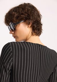 Czarna bluzka w paski z wysokim kołnierzem, z poziomymi prążkami w jasnoszarym kolorze oraz subtelnym detalem zapięcia z tyłu. W zestawie znajdują się dużych rozmiarów czarne okulary przeciwsłoneczne.