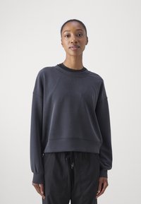 Sötét szürke pulóver laza szabással, kerek nyakkal és bordás mandzsettákkal. Puha tapintás minimalista varrásokkal és díszítésekkel. Fekete nadrággal párosítva.