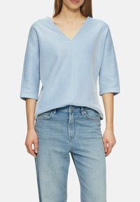 Blauw-witte gestreepte top met korte mouwen en een V-hals, met een losse fit en lichtgewicht stof. Gecombineerd met lichtblauwe jeans.