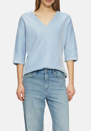Haut à rayures bleues et blanches, à manches courtes et décolleté en V, avec une coupe ample et un tissu léger. Associé à un jean bleu clair.