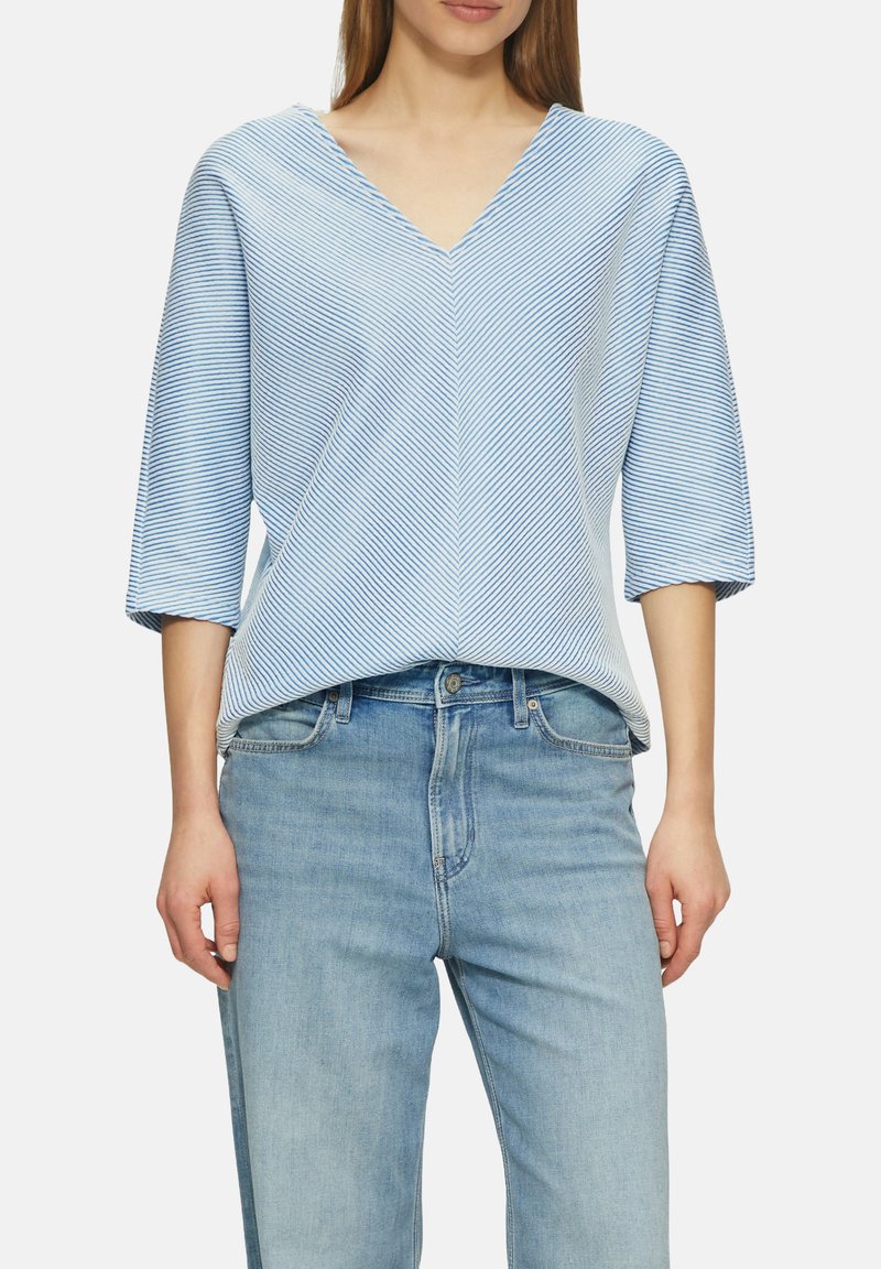 Blauw-witte gestreepte top met korte mouwen en een V-hals, met een losse fit en lichtgewicht stof. Gecombineerd met lichtblauwe jeans.