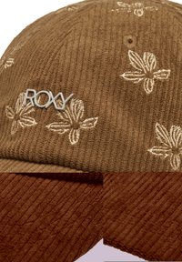 Bruine corduroy pet met geborduurd bloemenpatroon en zilveren "ROXY" logo. Kenmerkt zich door een gestructureerde oppervlakte en een contrasterende bruine rand.