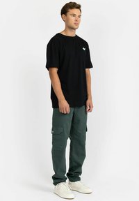 Black cotton t-shirt with short sleeves and a small turquoise logo, paired with green cargo pants featuring side pockets and a relaxed fit.