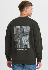 Mørkegrønn hettegenser med grafisk trykk av et luftfoto av en by; teksten under lyder "BLEND SINCE 1993." Langermet med ribbestrikkede mansjetter.