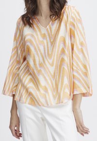 Blusa leggera e strutturata con scollo a V e maniche a tre quarti fluide. Il motivo presenta strisce ondulate nei colori arancione, rosa e crema.