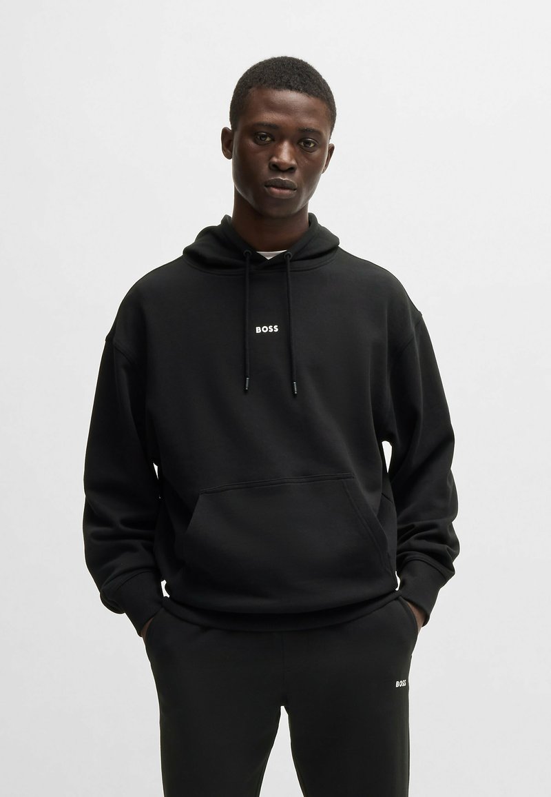 Svart huvtröja i mjukt tyg, med en framficka och en liten vit "BOSS"-logotyp på bröstet. Matchas med byxor i samma stil.