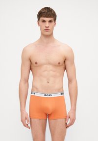 Orangene Boxershorts aus weichem Stoff, mit einem weißen Bund und schwarzem "BOSS"-Logo. Figurschnitt mit glatter Textur.