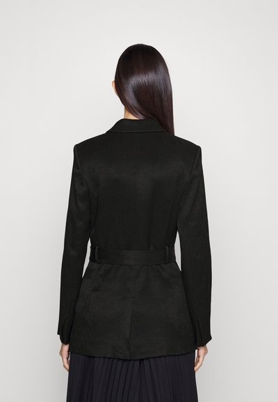 Zwarte op maat gemaakte blazer met een gladde textuur, voorzien van een ceintuurlengte en een gestructureerde kraag. De achterkant toont eenvoudige lijnen en naden.