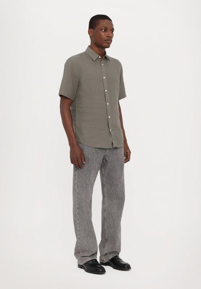 Korte mouwen, knoopsluiting shirt in gedempt groen, gemaakt van gestructureerde stof. Gepaarde met lichtgrijze, rechte jeans en zwarte schoenen.