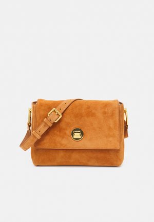 Sac bandoulière en daim couleur sable avec une bandoulière réglable et un fermoir rond doré sur le rabat avant.