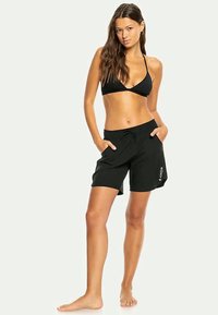 Juodas bikinio viršus ir juodos šortai su elastinga juosta, turintys šonines kišenes ir logotipo akcentą kairiajame kojoje.