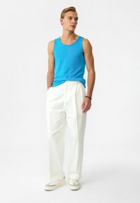 Blauwe tanktop van katoen, witte geplooide broek, witte sneakers en een armband om de pols. Schoon, minimalistisch ontwerp met een moderne pasvorm.