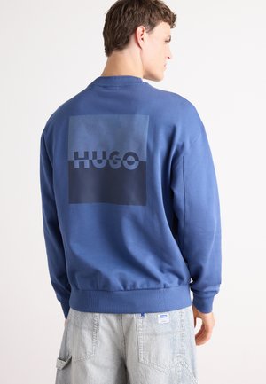 Blauw sweatshirt van katoen met een geribbelde ronde hals en manchetten. Voorzien van een groot donkerblauw rechthoekig logo met het woord "HUGO" op de achterkant.