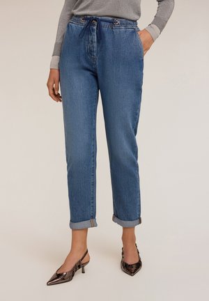 Lichtblauwe denim broek met opgerolde mouwen, elastische tailleband en trekkoord. Gecombineerd met glanzende, spitse zwarte hakken.