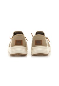 Zapatillas de tela beige con acentos marrones, suela de goma y lengüetas de agarre. Presenta una etiqueta de logo cosida en el talón y una textura suave.