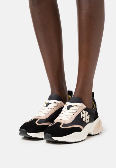 Sneakers har svart mocka och mesh med beige detaljer, tjock vit sula och en framträdande logotyp på sidan. Skosnören är krämfärgade.