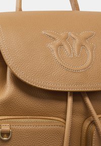 Zaino in pelle marrone chiaro con un classico coperchio arrotondato, decorato con uccelli ricamati, una superficie textured e una tasca frontale con zip in metallo dorato.