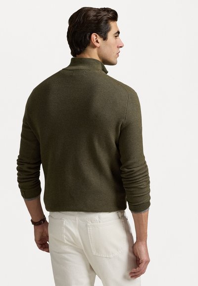 Pulover verde khaki cu guler înalt, tricotat texturat și manșete cu nervuri. Purtați-l cu pantaloni albi, care prezintă un model subtil și un material moale.