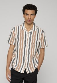 Chemise à manches courtes avec col, présentant un motif en zigzag aux couleurs marron, noir et blanc ; tissu léger avec une coupe décontractée.