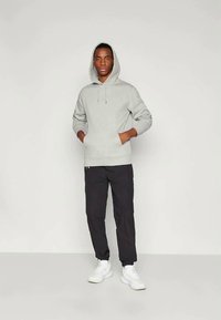 Γκρι φούτερ με τσέπη μπροστά και κορδόνια, σε συνδυασμό με μαύρα tapered παντελόνια και λευκά αθλητικά παπούτσια. Μινιμαλιστικός σχεδιασμός, χαλαρή εφαρμογή.