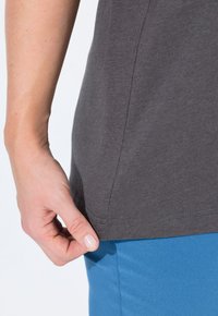 Orlo in cotone grigio, con un taglio semplice e un bordo arrotondato, abbinato a un tessuto blu sottostante. Primo piano di una mano che tiene la camicia.