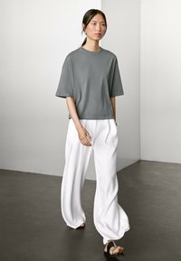 Grå oversized T-shirt med korte ærmer, parret med hvide vide bukser. Glat stof, afslappet pasform, minimalistisk design. Sorte sandaler.