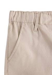 Beige bomullsbukser med elastiskt midjeband, med en sidoficka och prydlig sömnad, som visar upp ett mjukt, texturerat tyg.