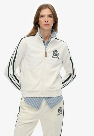 White zip-up jacket with green stripes; features embroidered logo on chest. Worn over a light blue striped shirt, paired with matching pants.