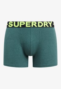 Boxers de color verde azulado con una cintura negra que presenta "SUPERDRY" en letras amarillas brillantes. Fabricados con una tela suave y texturizada.