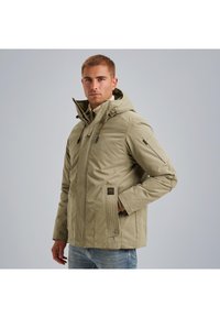 Svetlomodrý prešívaný kabát s kapucňou, s predným zipsom, bočnými vreckami a nastaviteľnými šnúrkami. Mäkka textúra, čisté línie a minimálne akcenty.