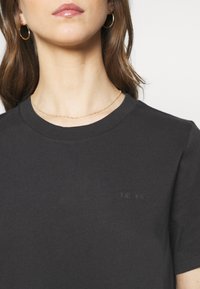 Mörkgrå bomulls t-shirt med rund halsringning, korta ärmar och en subtil logotryck på framsidan. Slät textur och figurnära design.