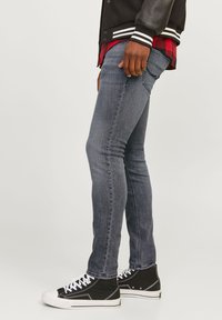 Lieknos džinsinės kelnės, pagamintos iš tamsiai mėlyno denim, su klasikiniu penkių kišenių dizainu, derinamos su juodais aukštais batais.