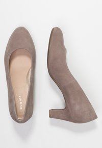 Chaussures à talons hauts en daim beige avec un bout arrondi, un talon bloc de hauteur moyenne et une doublure intérieure lisse. Présentent un design avec des découpes sur les côtés.