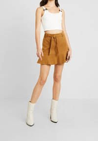 Top corto bianco a coste con spalline larghe e mini gonna in suede marrone con cintura annodata, orlo svasato e finitura testurizzata. Stivali bianchi alla caviglia.