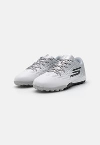 Athletic shoes in white and silver, featuring a textured upper, lace closure, and a black logo on the side. Rubber sole with traction.